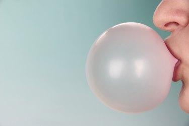 Person doing bubble with chewing gum on bright background