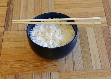 Bowl of white rice and chopsticks on wooden table