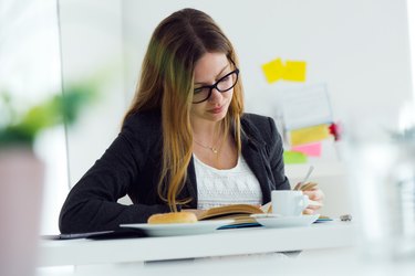 Young woman reading a book and having breakfast at home.