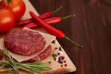 Raw meat for burgers with spices on wooden board