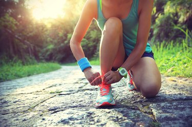 young woman runner tying shoelaces on stone trail