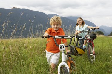 Boy and girl (5-8 years) with mountain bikes in long grass, smiling, portrait