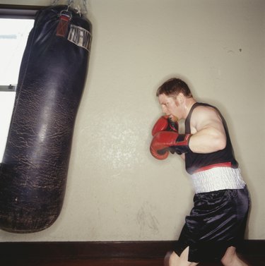 Boxer training with punch bag in gym, side view