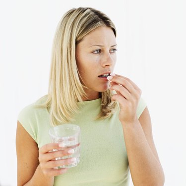 young woman holding a glass of water and taking a pill