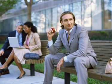 Side view of a businessman sitting on a bench and eating an apple