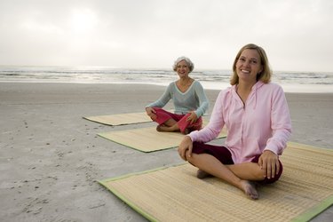 母亲与女儿锻炼一个垫子在海滩上