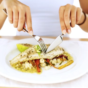 close-up of a woman's hands cutting a portion of food