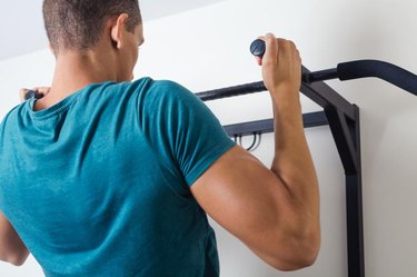 Muscular man doing pull ups at gym.