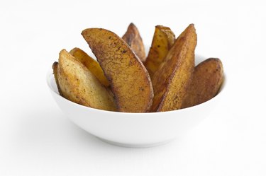 Potato wedges in a white bowl, studio shot