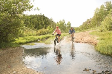 Women riding bicycles through mud pond