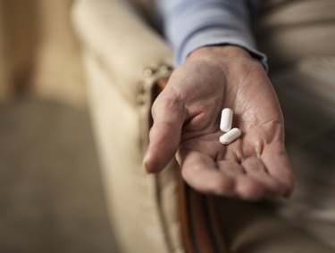 Senior woman holding two pills, close-up of hand