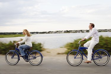 Couple riding bikes on road by water