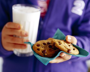 Child's hands holding cookies and milk