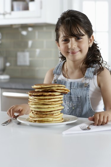 Girl (4-6) sitting at plate of pancakes, smiling, portrait