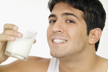 Smiling young man with milk mustache and holding glass of milk, close-up