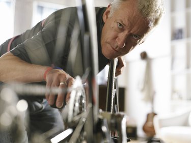 Mature man holding bicycle pedal, looking at wheel