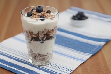 Healthy snack of blueberries, yogurt and granola parfait dessert layered in a clear glass.