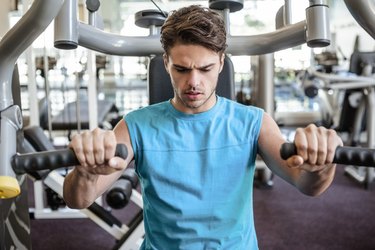 Focused man using weights machine for arms