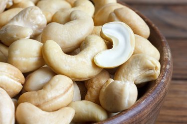 Wooden bowl of cashew nuts from above. On dark wood.