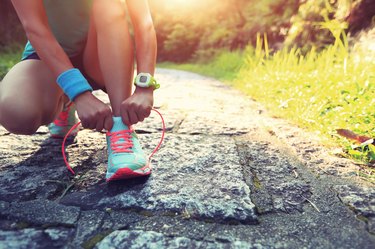 young woman runner tying shoelaces on stone trail