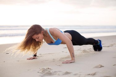 A woman exercises on the beach by doing push ups.