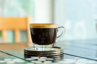 a cup of black coffee in a clear glass mug on a coaster