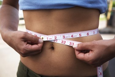 Mid section view of a woman measuring her waist with a tape measure