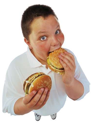 portrait of a young boy (10-14) holding a burger with one hand and eating a burger with the other