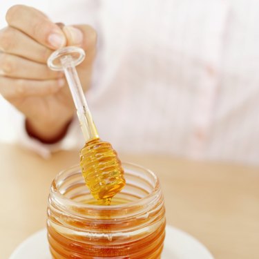 close-up of a woman's hand holding a honey dipper over a jar of honey