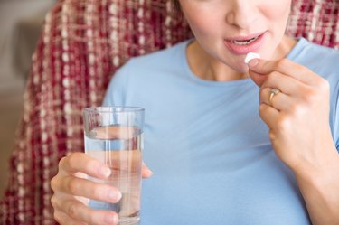 Pregnant person taking a vitamin tablet