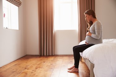 Pregnant Woman Sitting On Bed Holding Belly