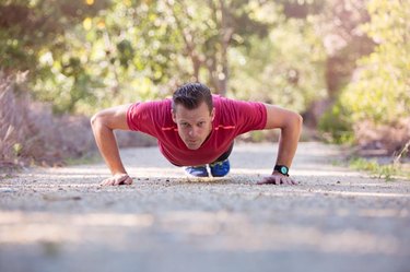 A determined young man does a pushup on a gravel footpath.