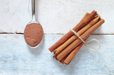 Cinnamon sticks tied next a spoon with powdered cinnamon