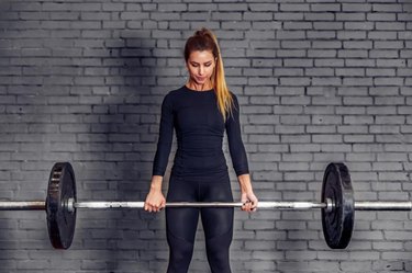 Young sports woman with weight barbell doing deadlift exercise. Fit female athlete in great shape is lifting weights in a sport gym. Athletic woman train gym workout.