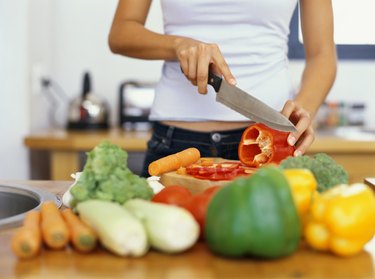 mid section view of a young woman cutting red bell pepper in the kitchen