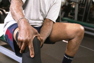 Senior man in gym wearing knee strap, holding knee, close-up