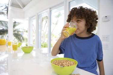 Boy (8-10) at table, drinking orange juice