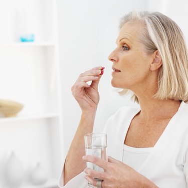 Side view of mature woman holding glass of water and taking pills