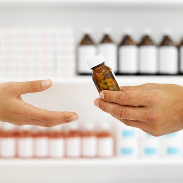Close up of the hands of a pharmacist giving a patient a bottle of pills