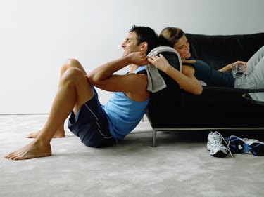Couple wearing sports clothes resting in living room, smiling