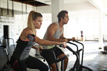 Woman & man working out on crosscycle at gym