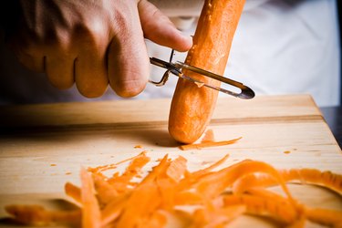 Close-up of hand peeling raw carrot on wooden cutting board