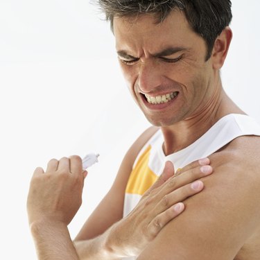 side profile of a mid adult man applying ointment on his shoulder