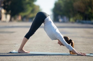 Yoga in the city: beautiful young sporty woman wearing sportswear working out on the street on summer day, doing downward facing dog posture, full length, profile view