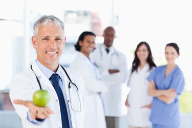 Mature doctor holding an apple while his medical team is looking at him