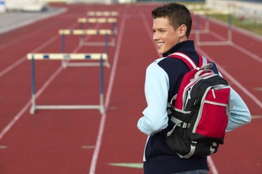 teenage boy (16 -18) wearing a backpack walking on a running track