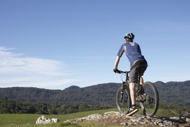 Man on mountain bike standing at edge of rock, looking at landscape, rear view