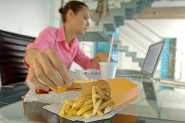 Businesswoman eating French fries, using laptop