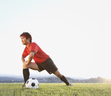 Man stretching in field with soccer ball