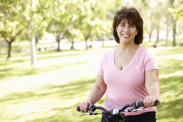 Older person smiling while riding a bicycle in a park.
